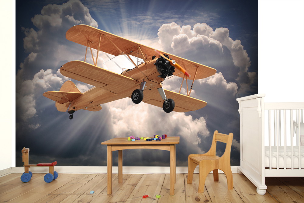 Fototapete - Doppeldecker-Flugzeug fliegt durch dramatische Wolken über einem Kinderzimmer mit Holzmöbeln