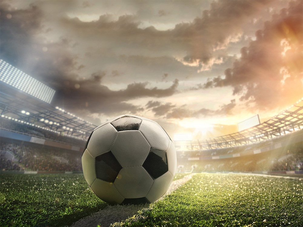 Fototapete - Ein Fußball liegt auf einem Stadionrasen bei Sonnenuntergang