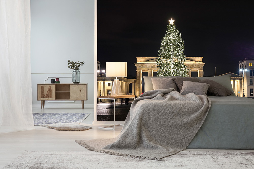 Wall mural - Cosy bedroom with a view of an illuminated Christmas tree and a historic building in the background