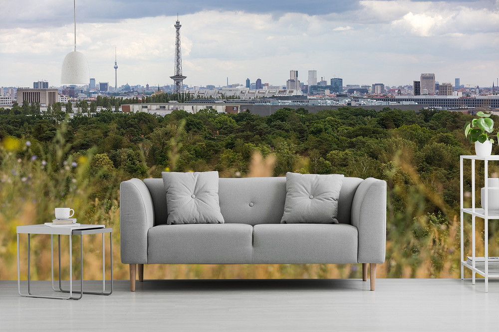 Muurschildering - woonkamer met grijze bank voor panorama van stad en bos op de achtergrond
