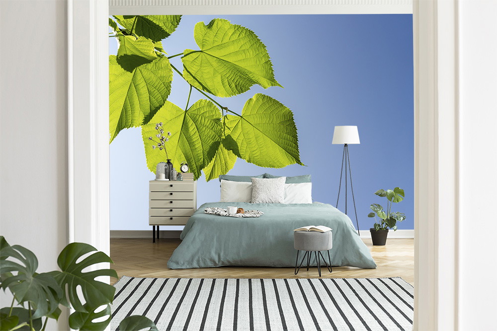 Fotobehang - Stijlvolle slaapkamer met grote wanddecoratie van groene bladeren op een blauwe achtergrond