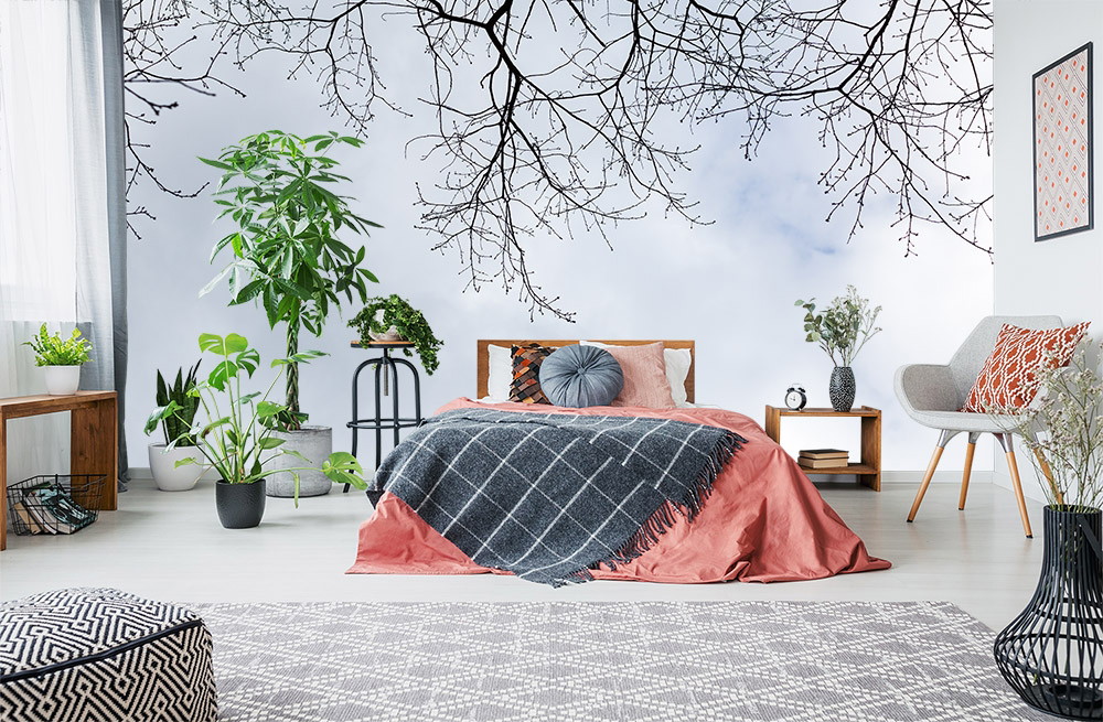 Fototapete - Schlafzimmer mit rosa Bettwäsche, blattlosem Baum als Wandbild und grünen Pflanzen.