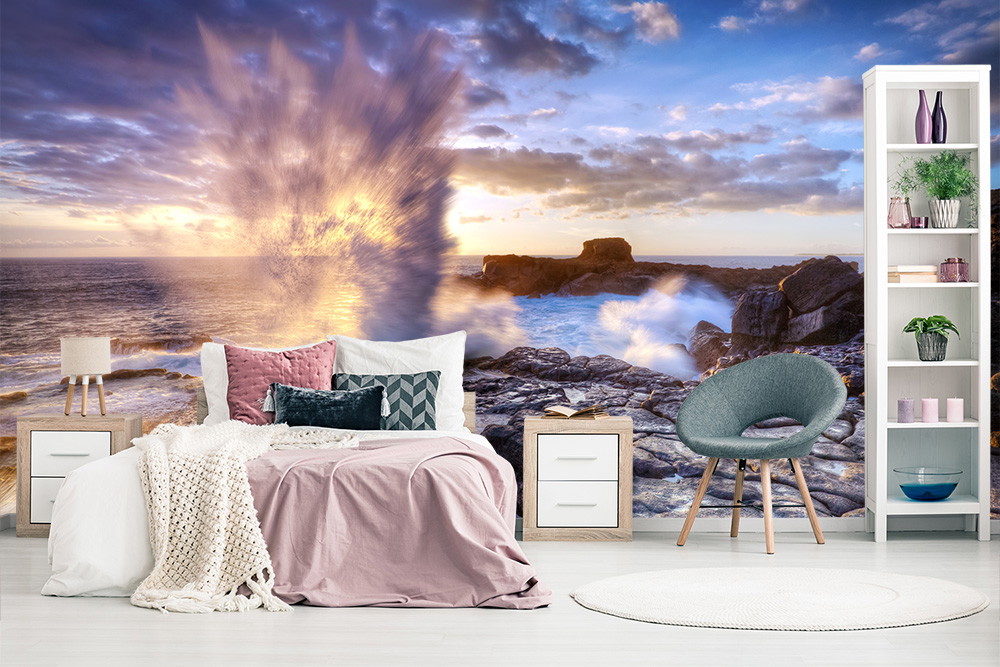 Wall mural - Elegant bedroom with wall mural of waves crashing against rocks as the sun sets on the horizon