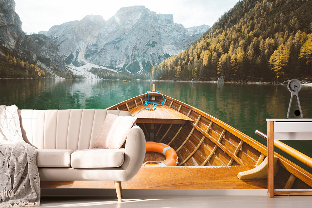 Wall mural - A wooden boat sailing on a calm lake, surrounded by majestic mountains and forests