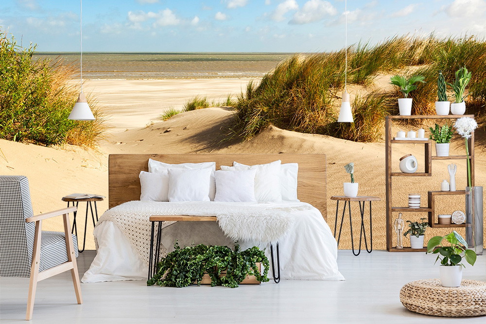 Fototapete - Schlafzimmer mit Bett, Pflanzen und Wandbild einer Strandlandschaft mit Dünen